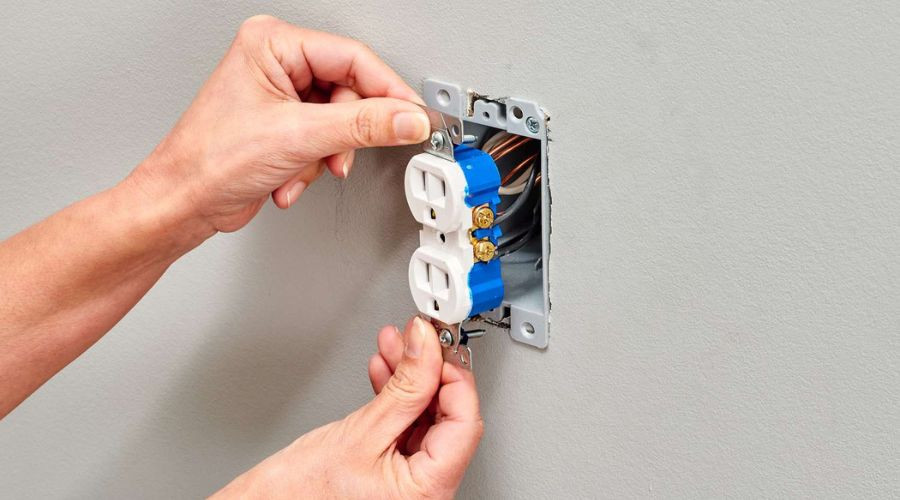 Person's hands performing electrical work on a dual socket outlet for Trustworthy Electric services.