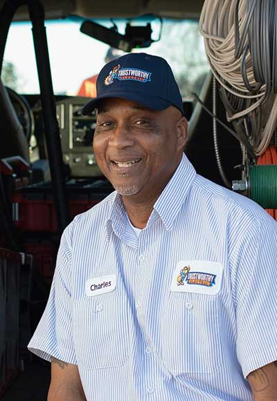 Charles, technician at Trustworthy Electric, smiling in uniform with company logo, standing beside a service vehicle interior.